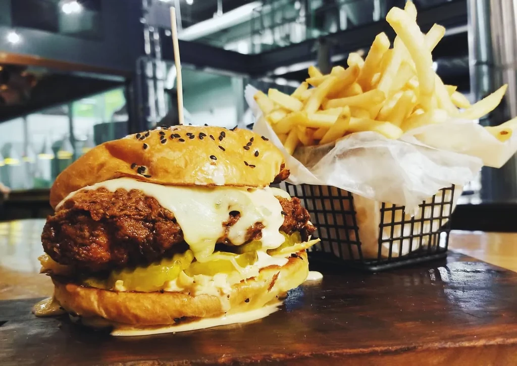 Fried chicken sandwich, fries, and sauce on a dark wooden board.