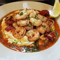Shrimp and grits dish with red sauce, green herbs, and lemon.