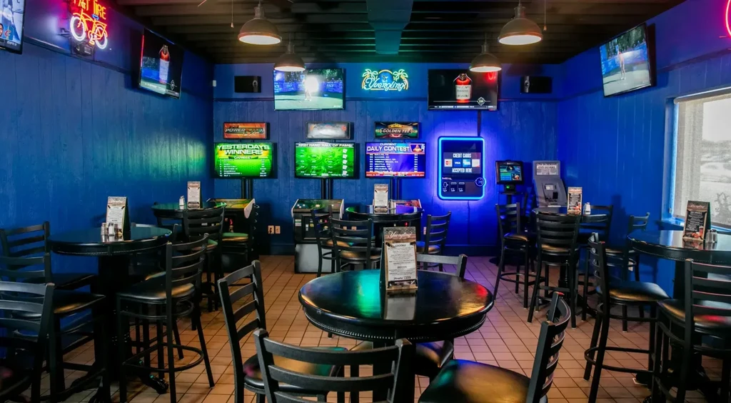 Casual bar with blue walls, high-top tables, TVs, and neon signs.