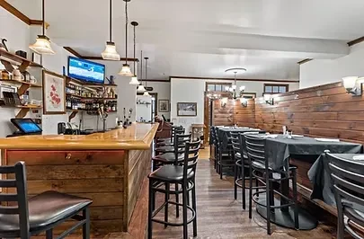 Well-lit, empty restaurant with a rustic wooden bar and dining tables.
