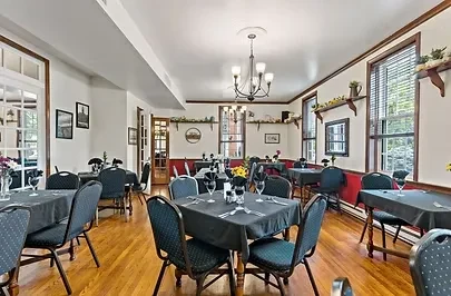 Empty restaurant dining room with set tables, red wainscoting, and wooden floors.