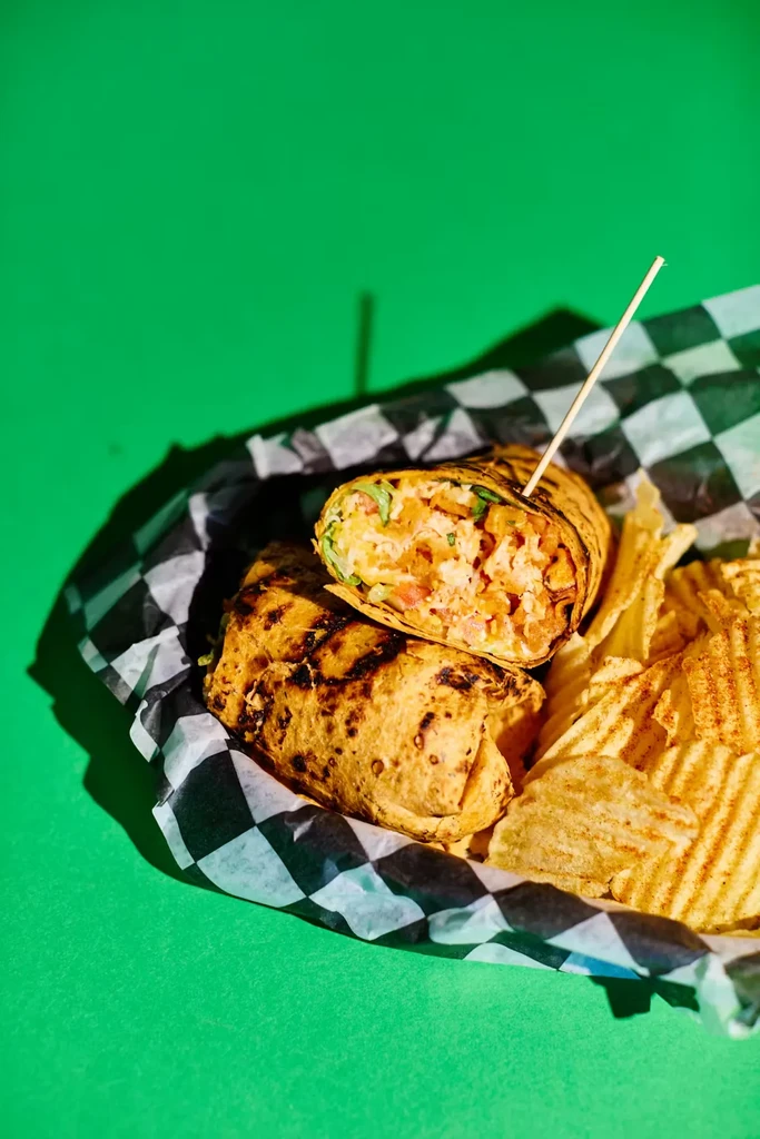 Halved grilled wrap with chicken, veggies, and chips in liner.