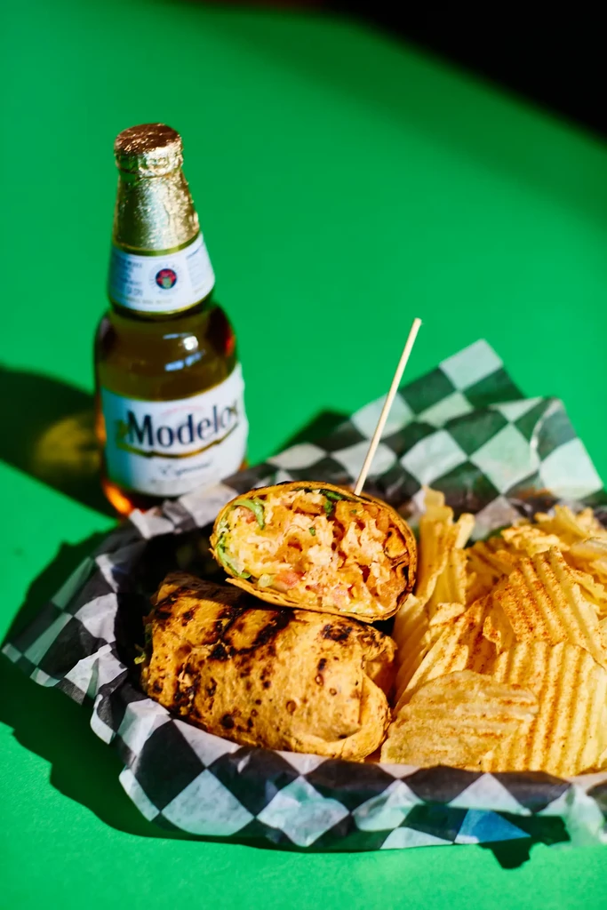 Savory grilled wrap, crinkle chips, and Modelo beer on green.