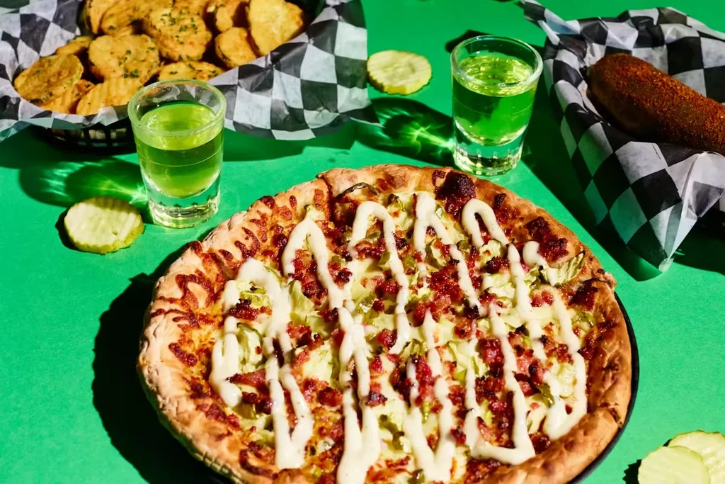 Still life of pizza, fried pickles, and green shots on a green background.