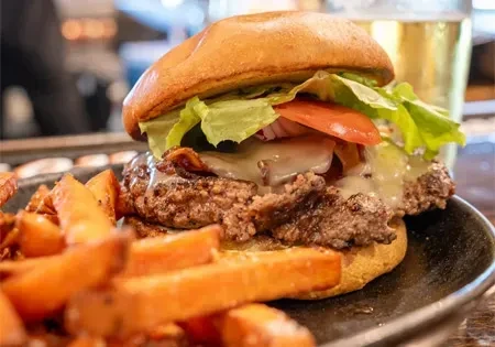 Gourmet beef burger with melted cheese, bacon, and sweet potato fries.