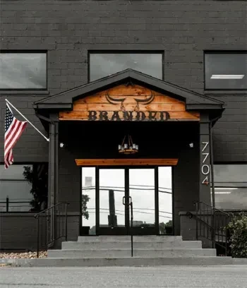 Dark brick building entrance with 'BRANDED' bull skull sign and American flag.
