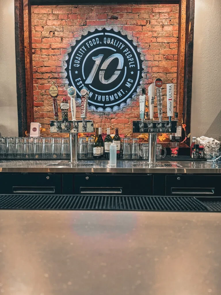 Rustic bar area with beer taps, inverted glasses, and a '10' sign.