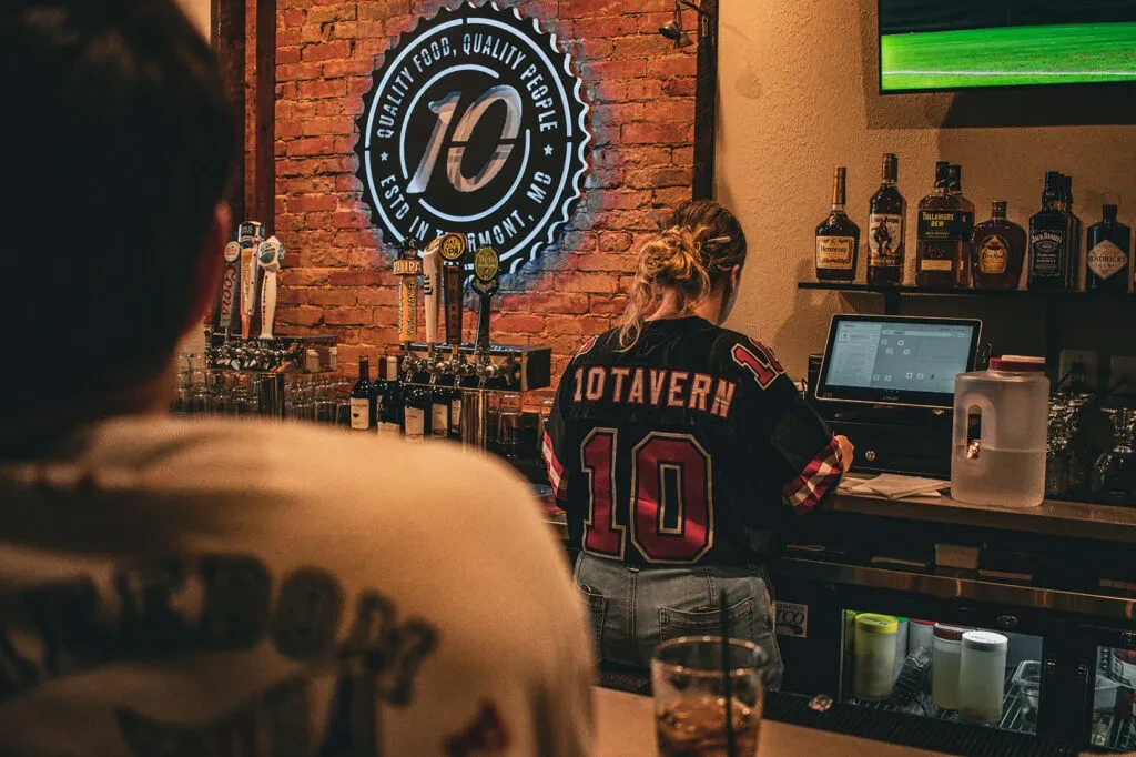Warm tavern bar with bartender, neon sign, and beer taps.