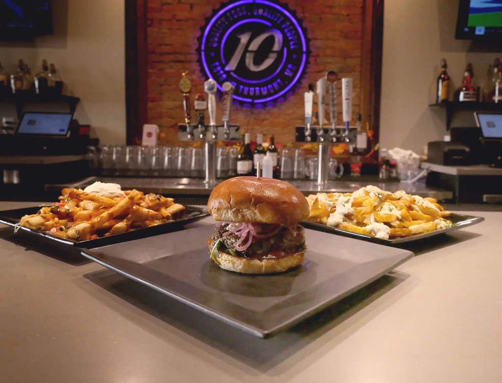 Gourmet burger, cheese fries, and sauced fries on a bar counter.