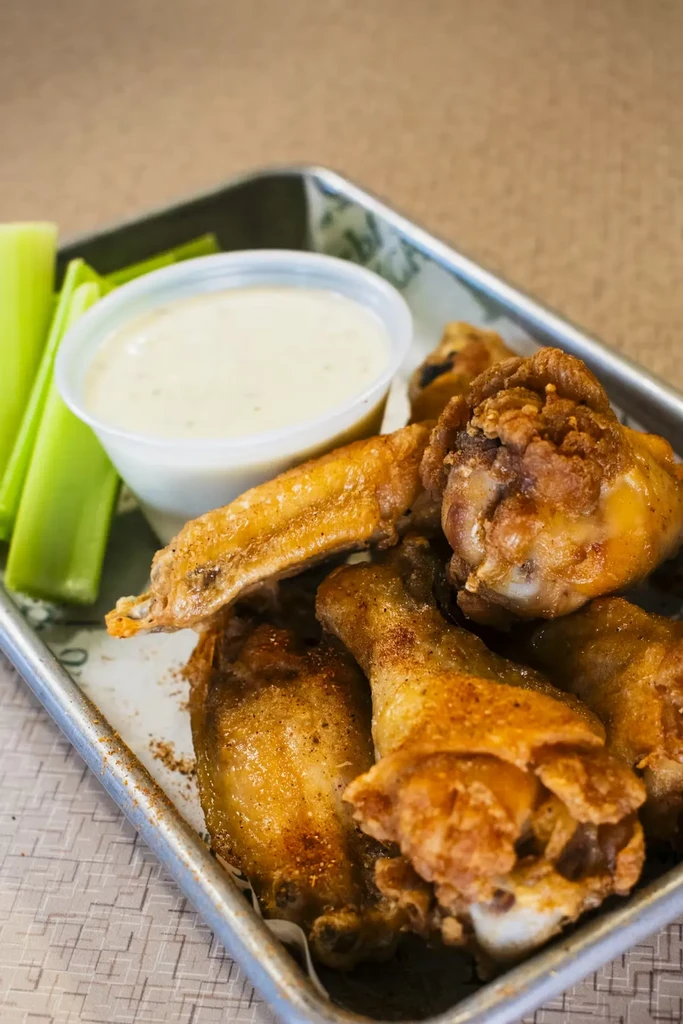 Golden-brown fried chicken wings with celery and creamy dip.