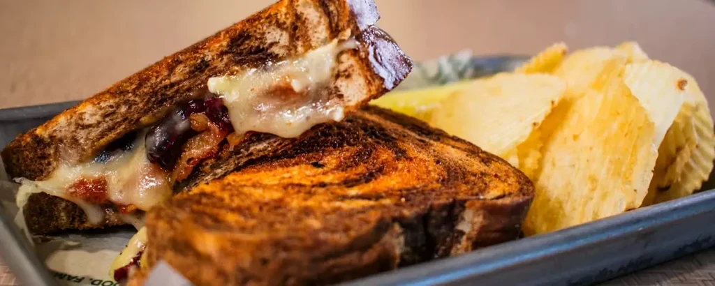 Grilled sandwich with melted cheese and chips on a dark tray.