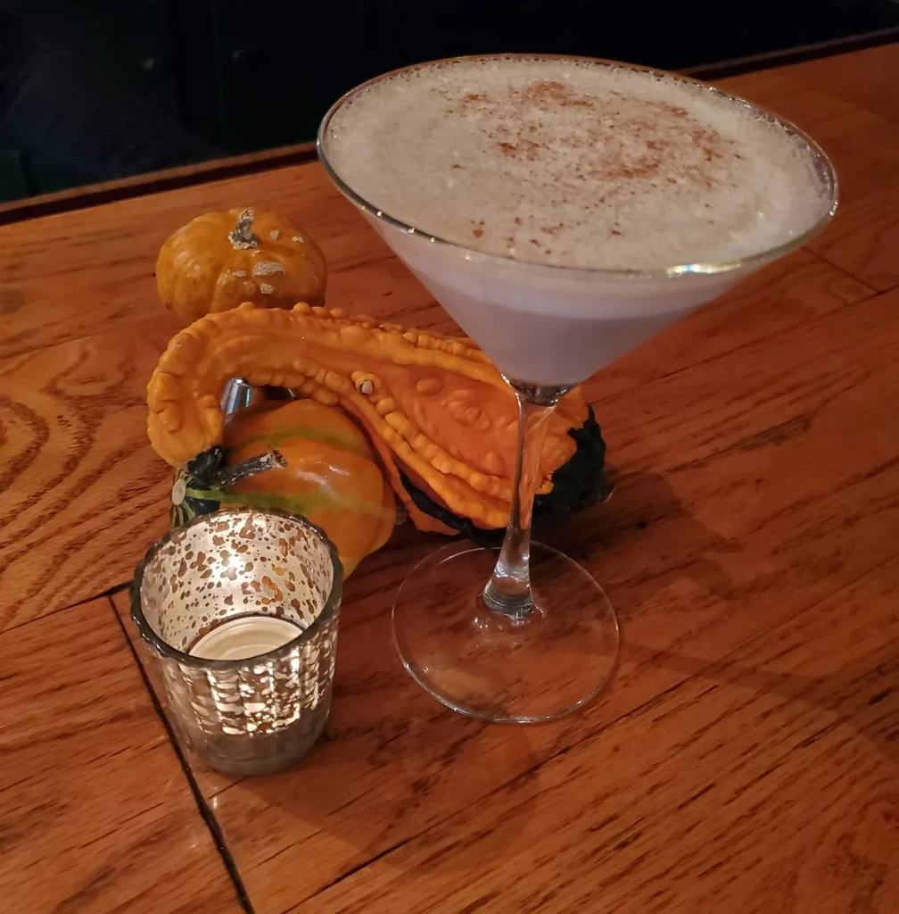 Martini glass with frothy purple drink, spice, pumpkins, and lit candle.