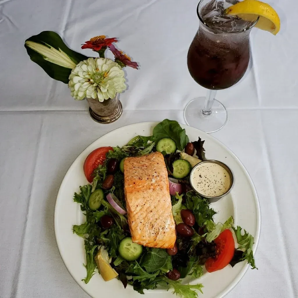 Top-down view of salmon salad, dressing, beverage, and flowers.
