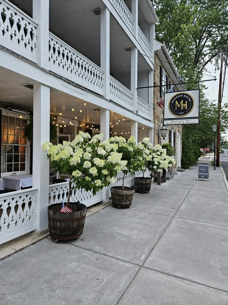 Mansion House Inn with white ornate balconies, hydrangeas, American flag.
