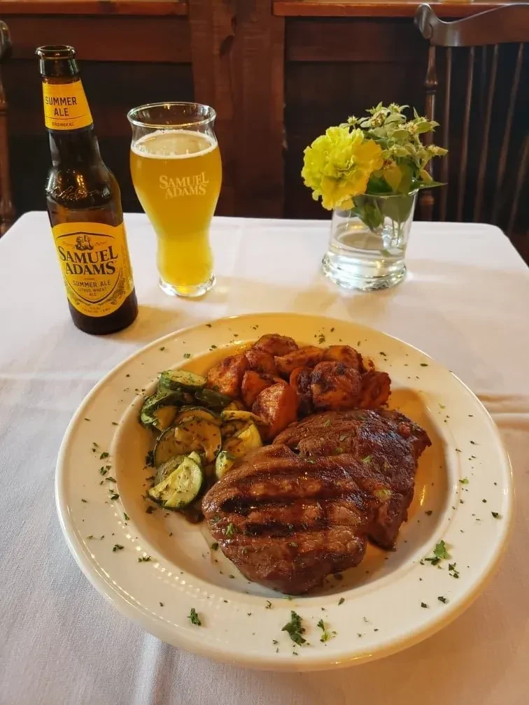 Grilled steak dinner with Samuel Adams beer and yellow flowers.