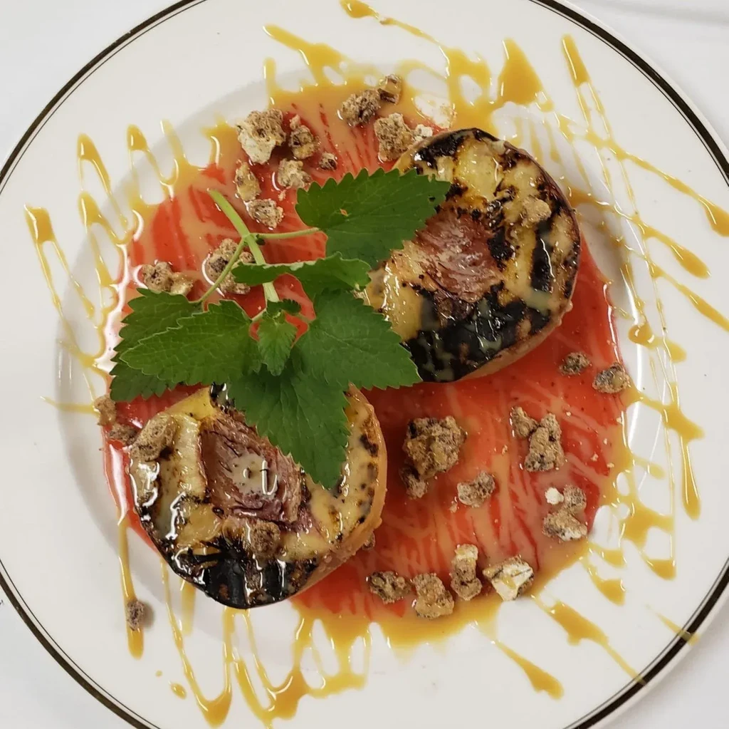 Grilled fruit, cream-filled, with berry sauce, crumbles, and caramel drizzle.