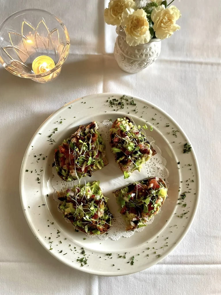 Four vegetable bruschetta, lit candle, flowers on a white tablecloth.