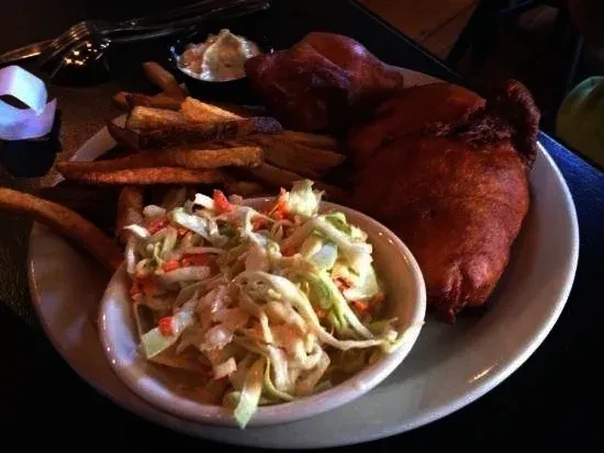 Plate of deep-fried food, thick-cut fries, coleslaw, and dipping sauce.