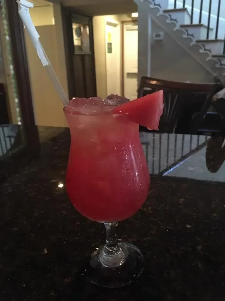 Vibrant red beverage in hurricane glass with ice, watermelon, and straw.