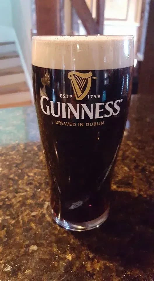 Full pint of Guinness stout, creamy white head, logo on glass.