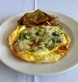 Golden omelet with cheese, herbs, and crispy potatoes on a plate.