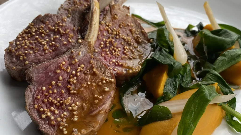 Three medium-rare lamb chops with green and orange vegetables on a white plate.