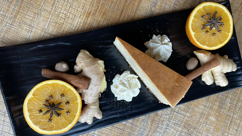 Spiced cheesecake slice with cream, ginger, cinnamon, nutmeg, orange on wood.