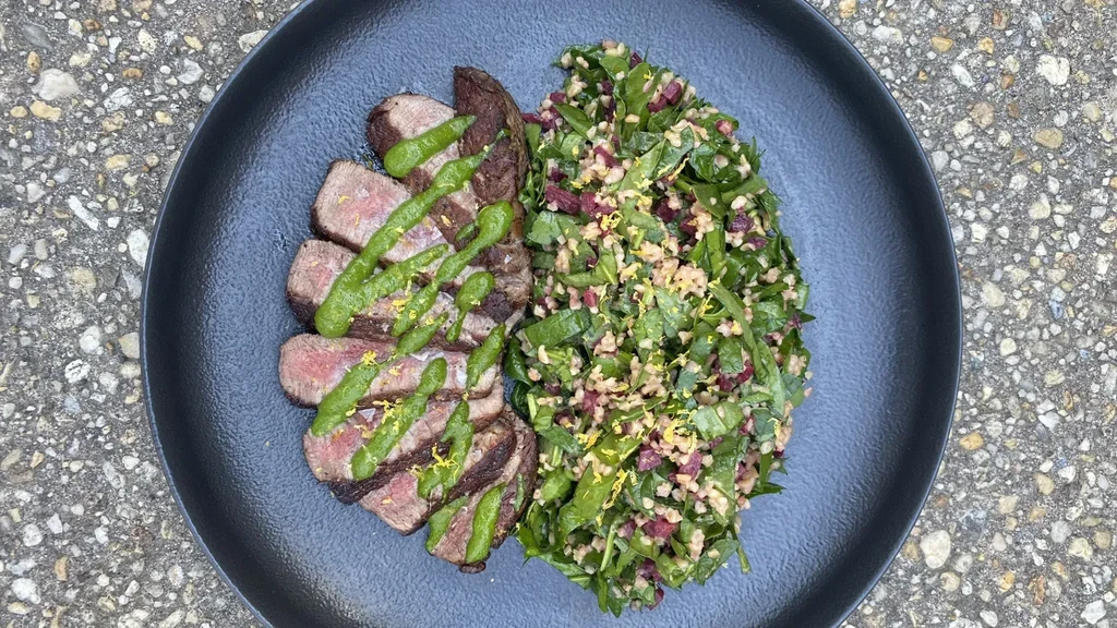 Overhead of medium-rare steak, green sauce, and colorful grain salad.