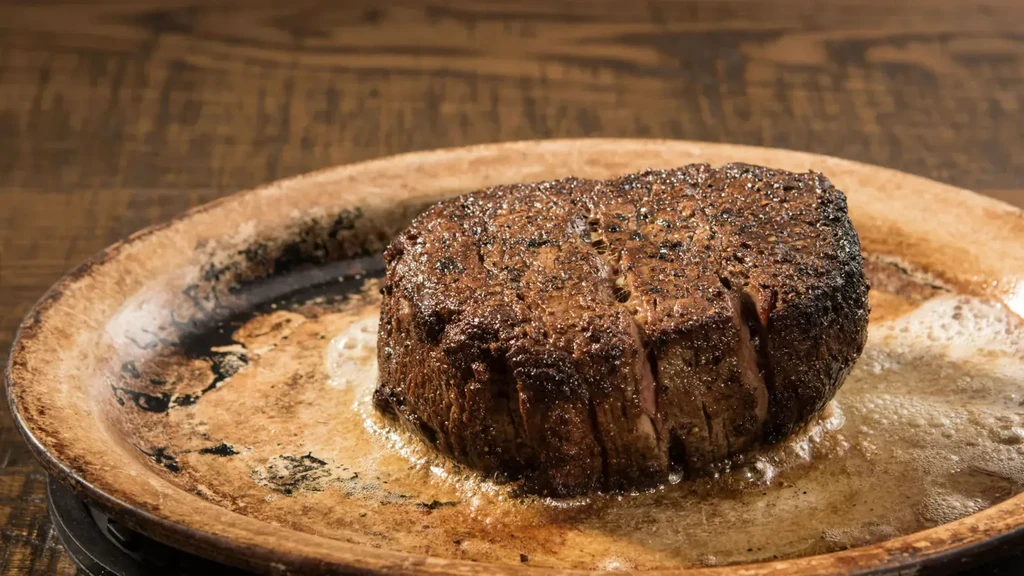 Seared steak with dark crust, bubbling fat, in a rustic pan.