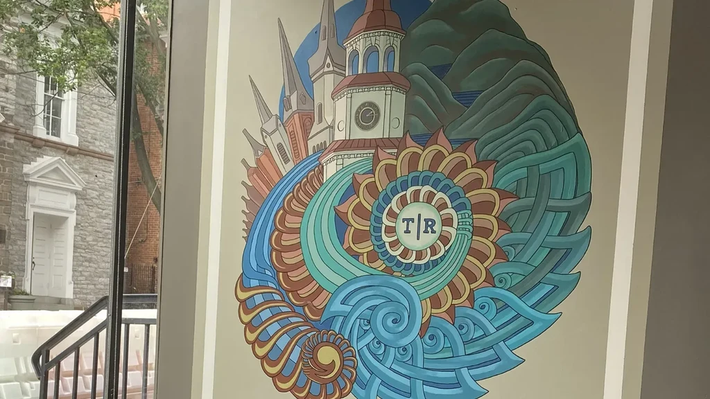 Vibrant intricate mural with churches, nature, and "T|R" emblem, beside a window.