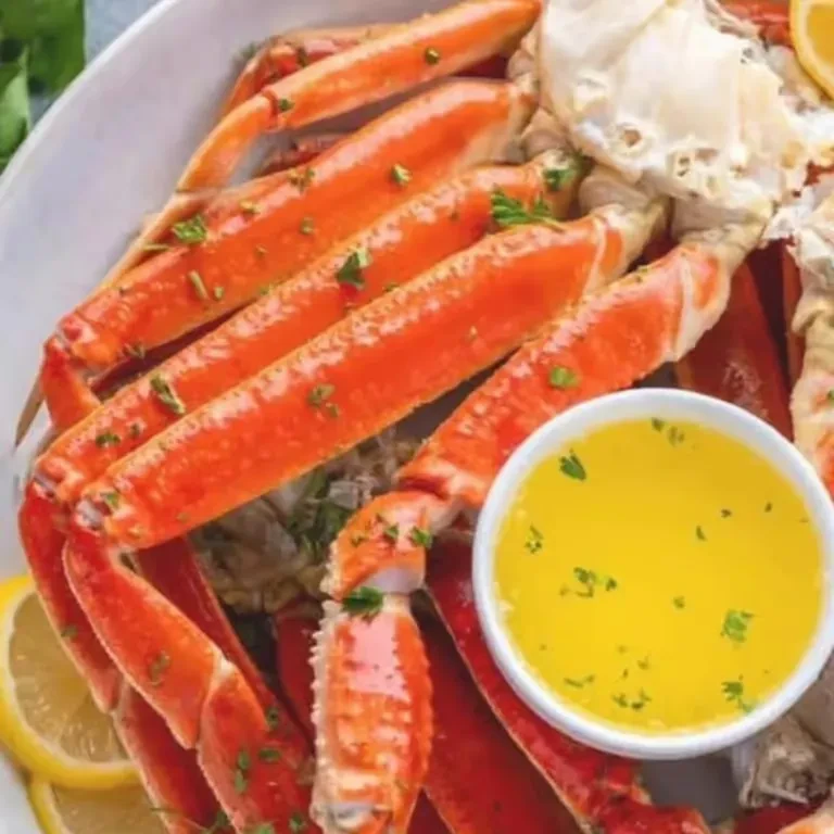 Platter of cooked orange-red crab legs with melted butter, lemon, herbs.