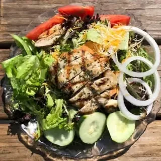 Overhead grilled chicken salad with lettuce, tomato, cheese, cucumber, onion.