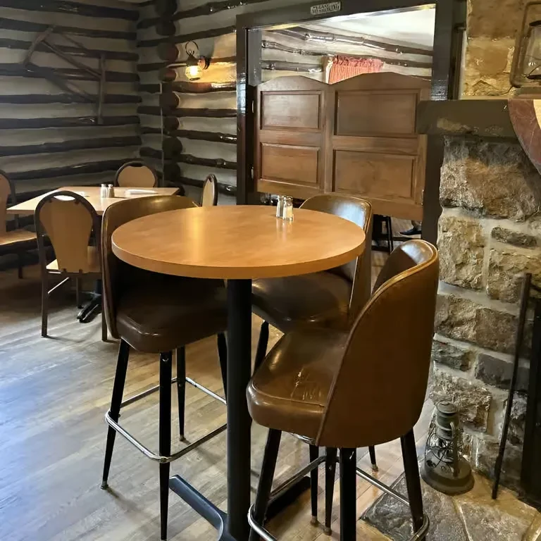 Rustic bar interior with high-top table, leather stools, and log walls.