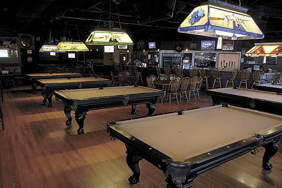 Dim pub interior with ornate pool tables and a fully stocked bar.