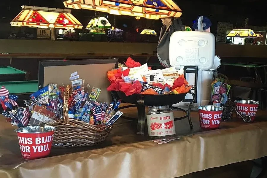 Bar event table with flags, Budweiser bucket, donation jar, and raffle.