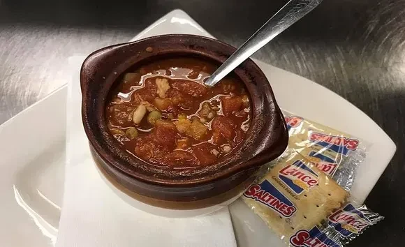 Rustic bowl of reddish-brown stew, spoon, and saltine crackers.