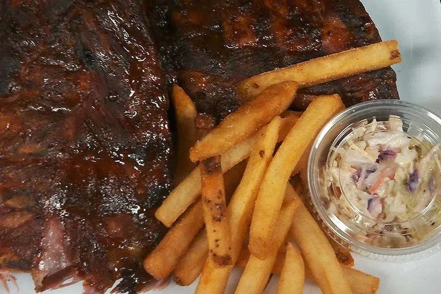 Plate of barbecue ribs, crispy fries, and coleslaw in a cup.