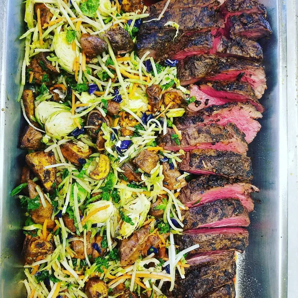 Metal tray with grilled steak slices and colorful roasted vegetable medley.