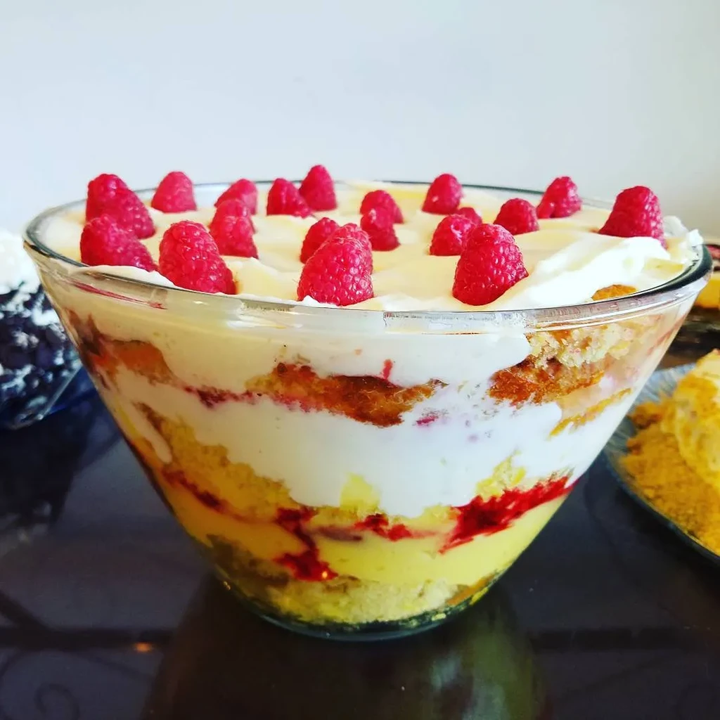 Layered dessert with yellow cake, custard, raspberry, and cream.