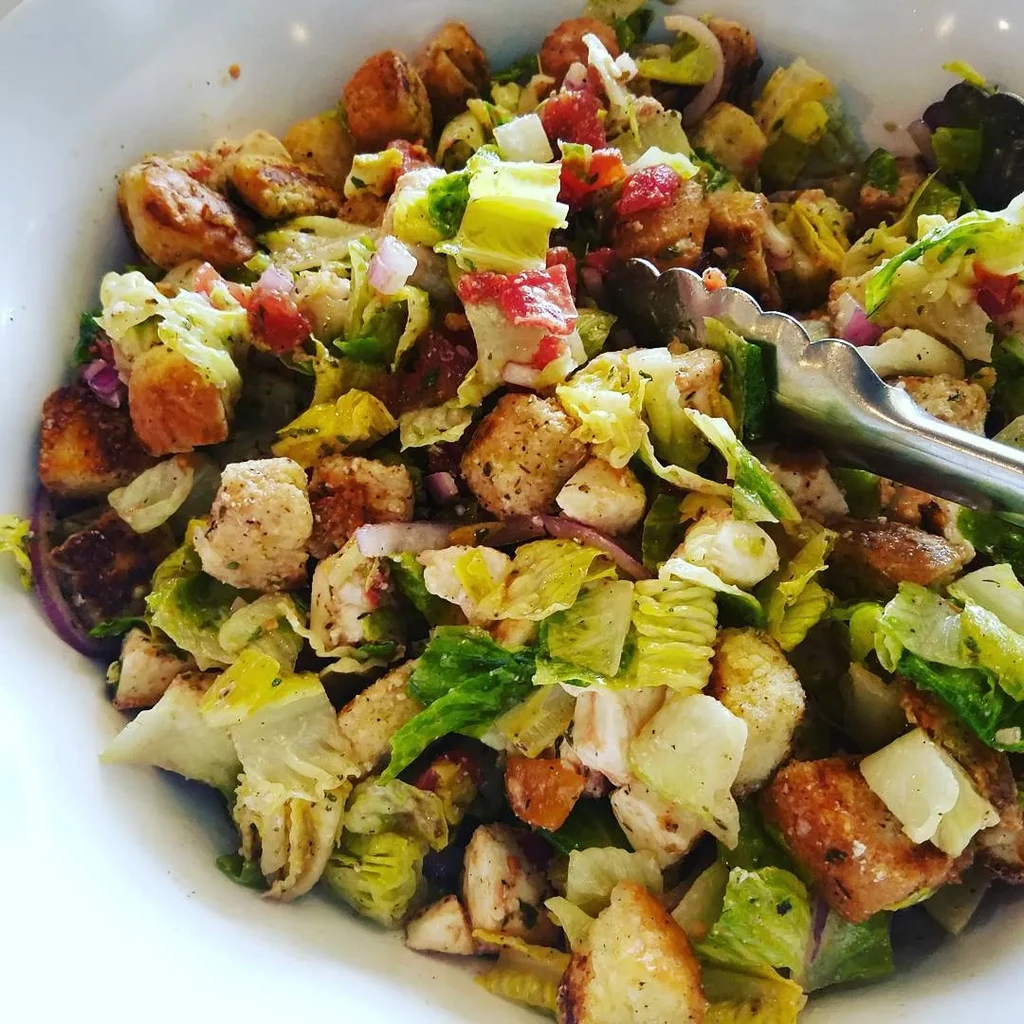 Mixed chicken salad with croutons, vegetables, and serving tongs.