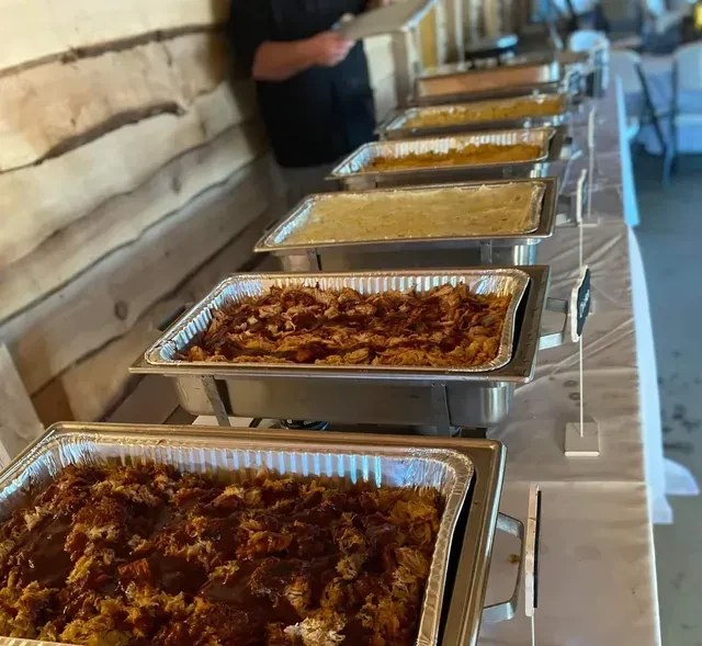 Buffet line featuring chafing dishes with shredded meat and other food.
