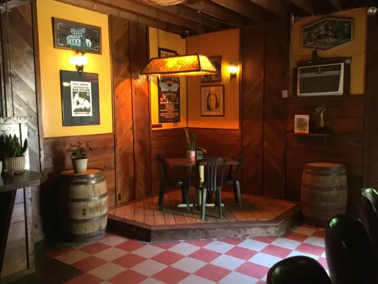 Warm, rustic bar interior with dark wood, stained glass lamp, and barrels.