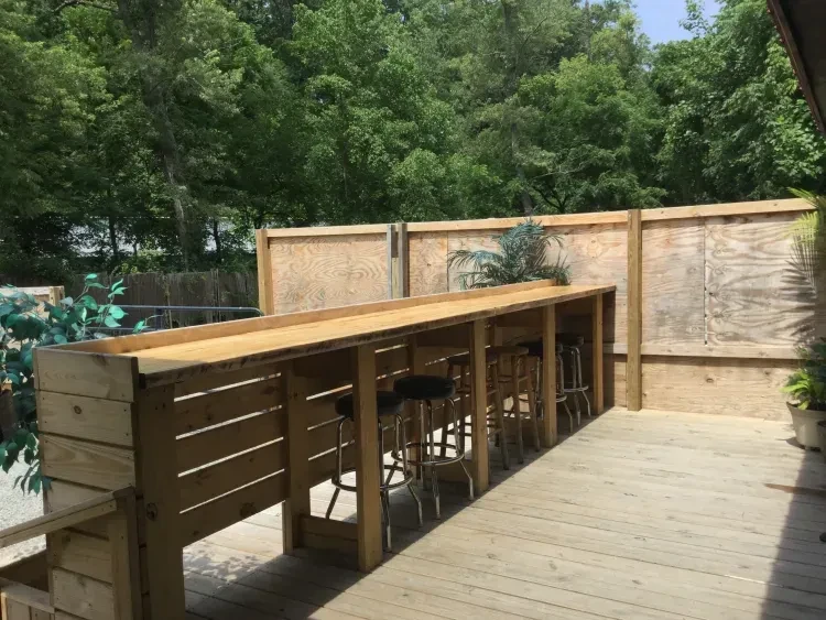 Rustic outdoor wooden bar with stools and greenery.