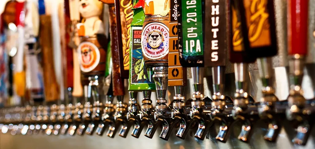 A long row of uniquely branded beer tap handles at a bar.