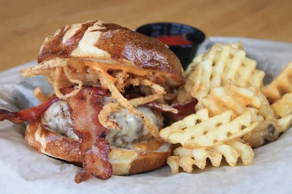 Pretzel bun burger, bacon, onion strings, waffle fries, and ketchup cup.
