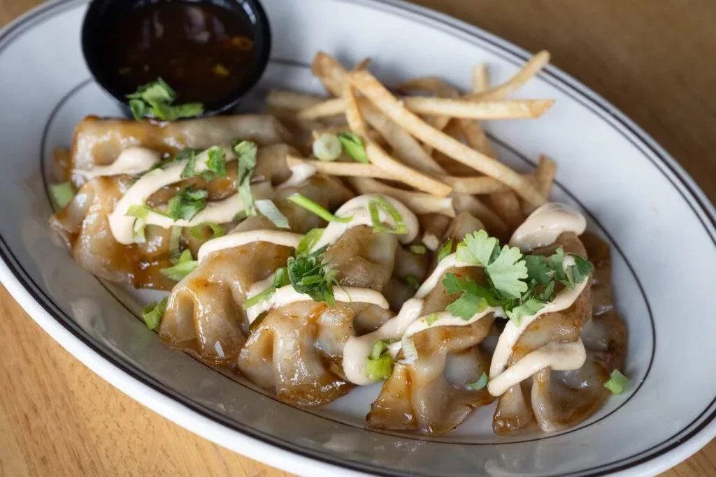 Pan-fried dumplings with creamy sauce, green onions, fries, and dipping sauce.