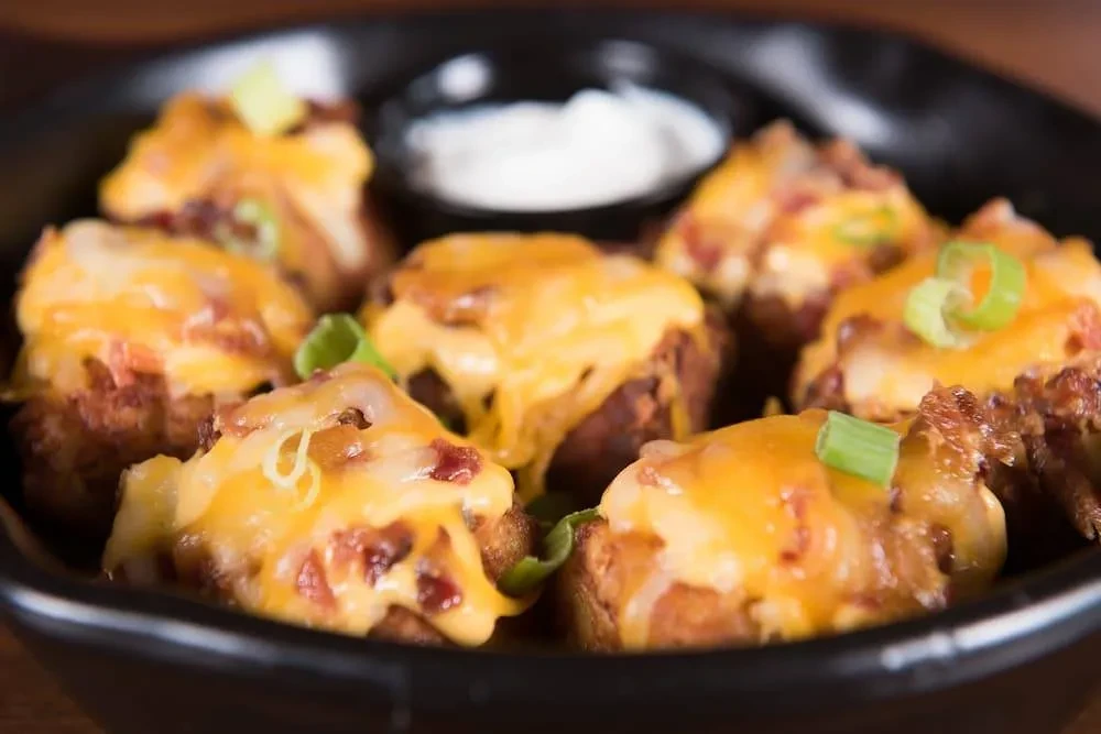 Loaded potato bites with melted cheese, bacon, green onions, and dip.