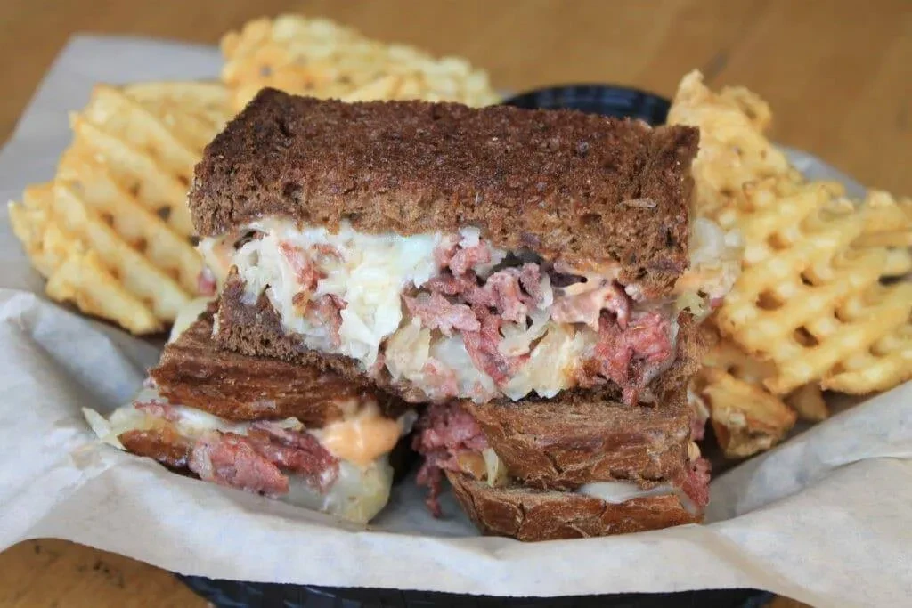 Stacked Reuben sandwich on rye bread with a side of waffle fries.