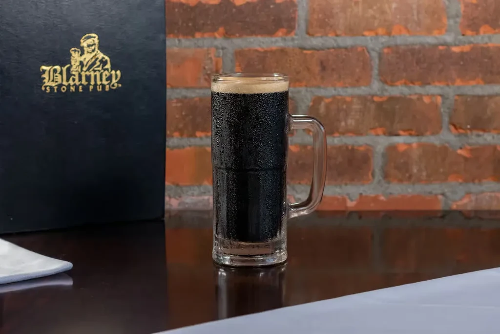 Cold, frothy beer mug, Blarney Stone Pub menu, rustic brick wall.
