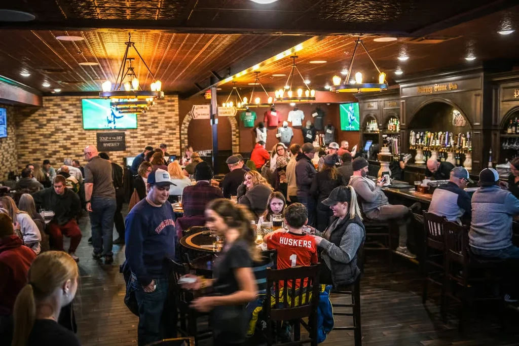 Lively pub interior with exposed brick, a long bar, and many patrons.